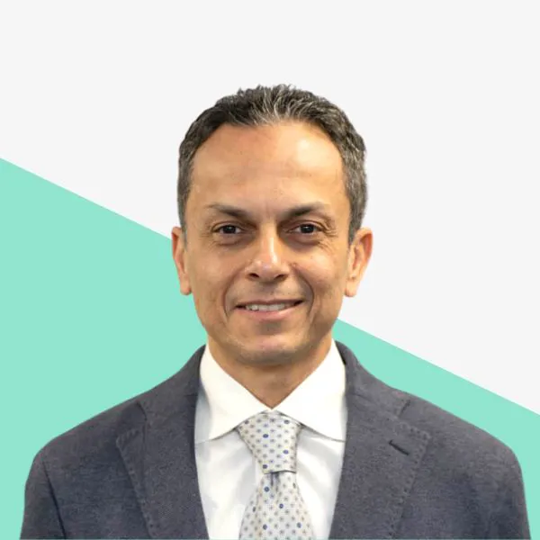 Smiling man in a dark suit against a light background with a teal diagonal.