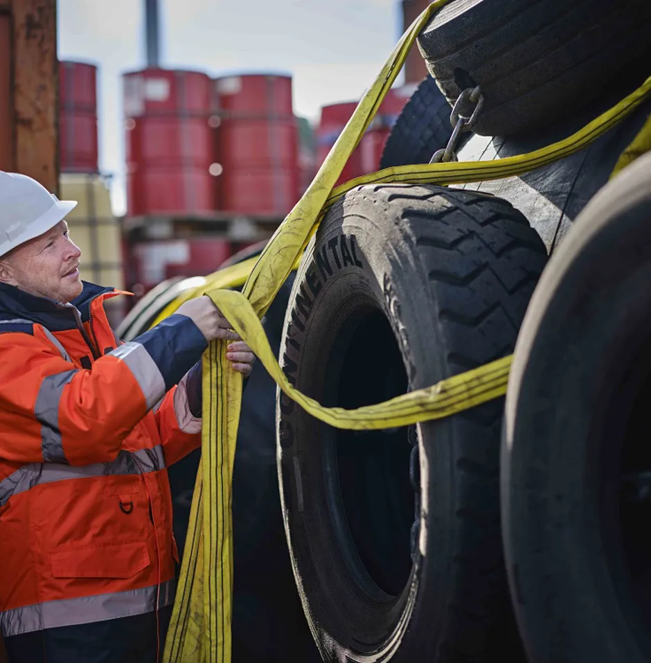 Worker securing tires with straps in storage.