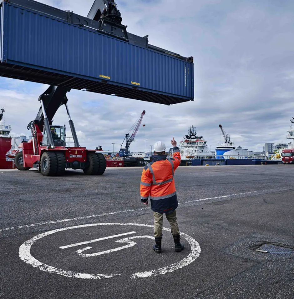 Worker signals as a container is lifted at port.
