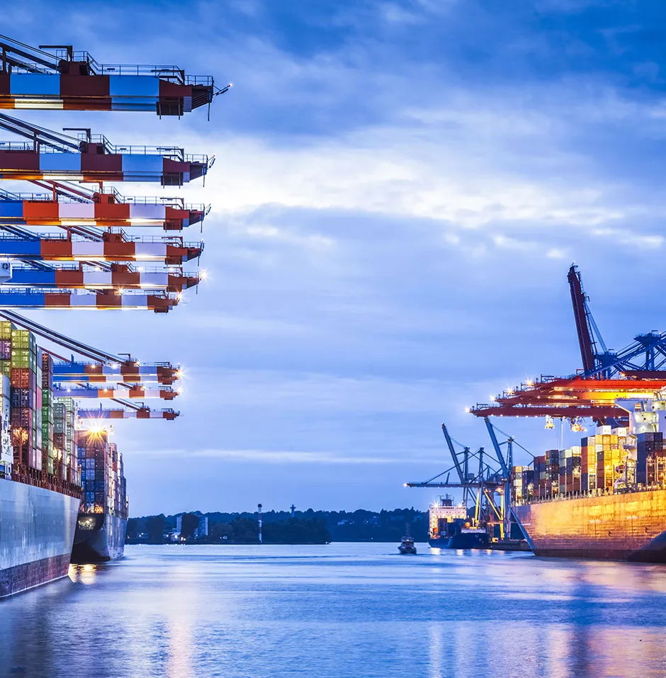 Vibrant port scene at dusk with moored container ships, cranes, and stacked containers.