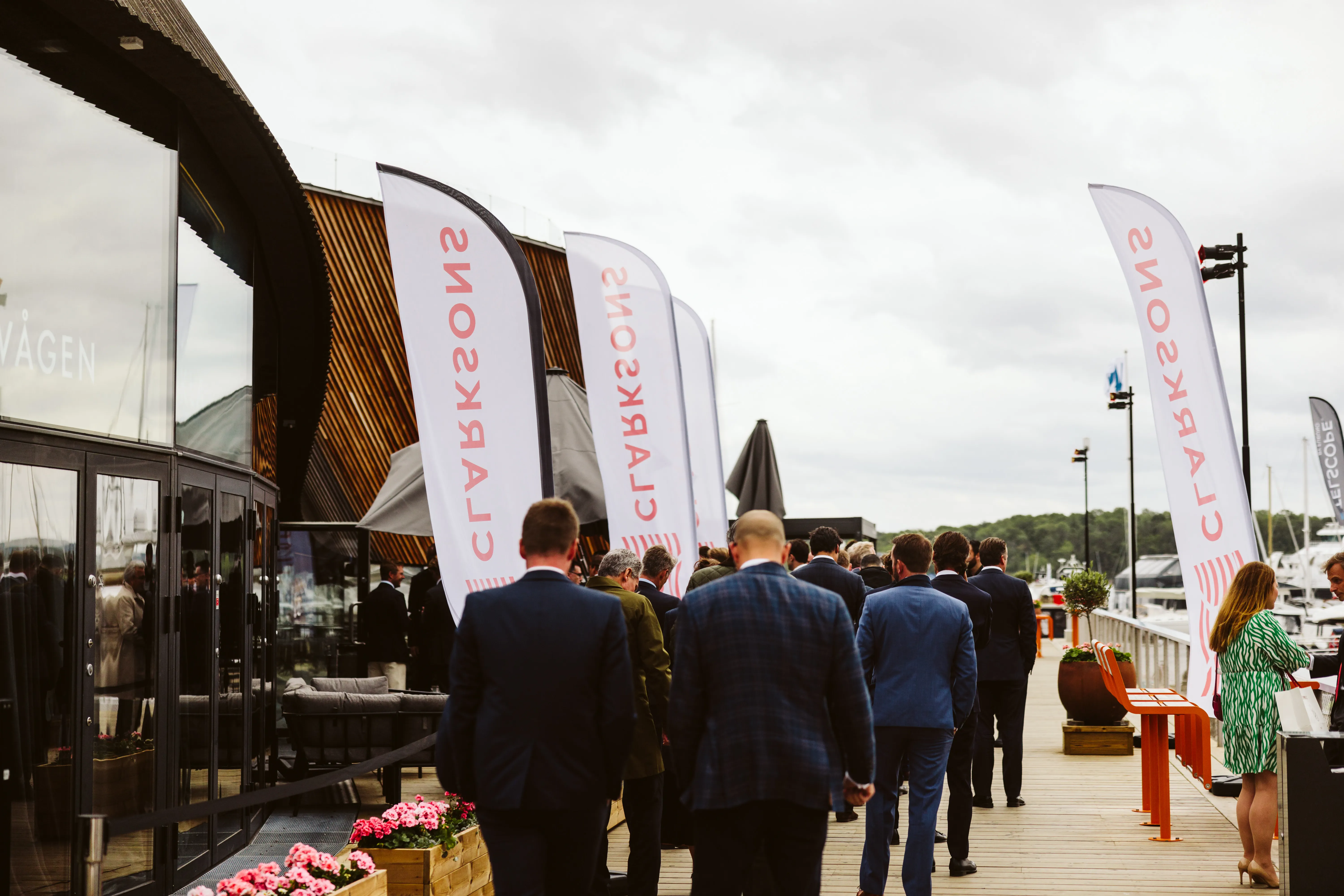 Group in formal attire walking on a deck beside a marina with CLARKSONS flags.