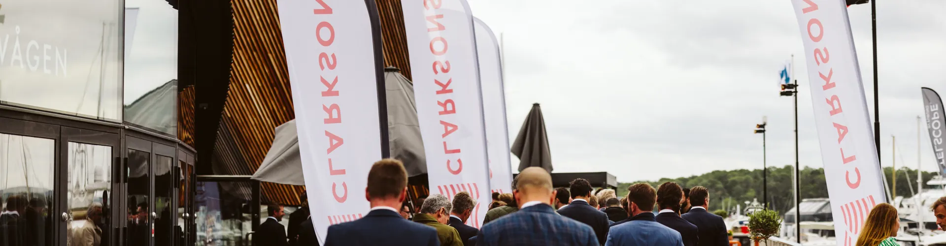 Group in formal attire walking on a deck beside a marina with CLARKSONS flags.