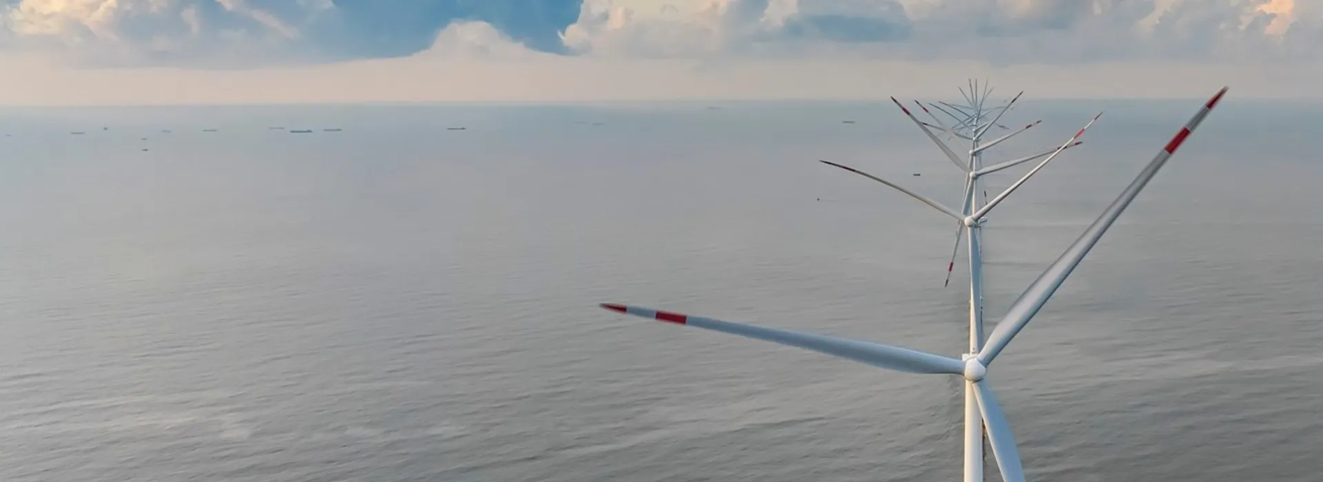 Aerial view of an offshore wind turbine with boats visible on the horizon.