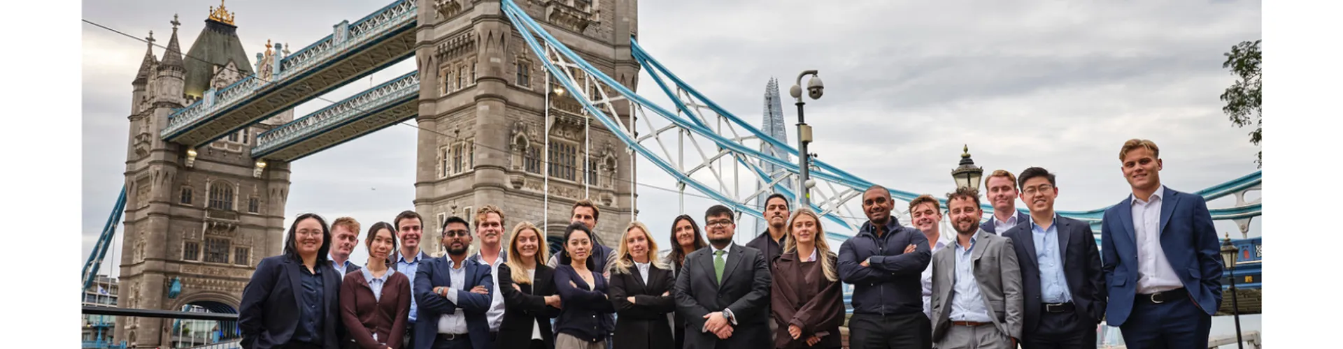 Diverse group of people in business and casual attire standing in front of London's Tower Bridge.