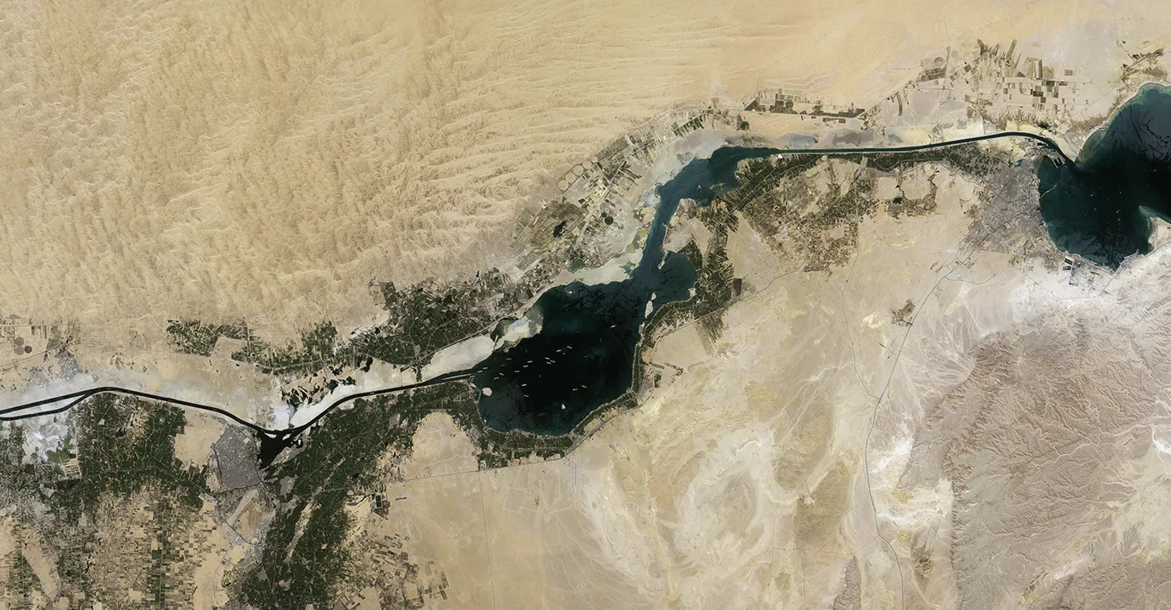 Aerial view of desert landscape intersected by a dark blue river with green agricultural land.